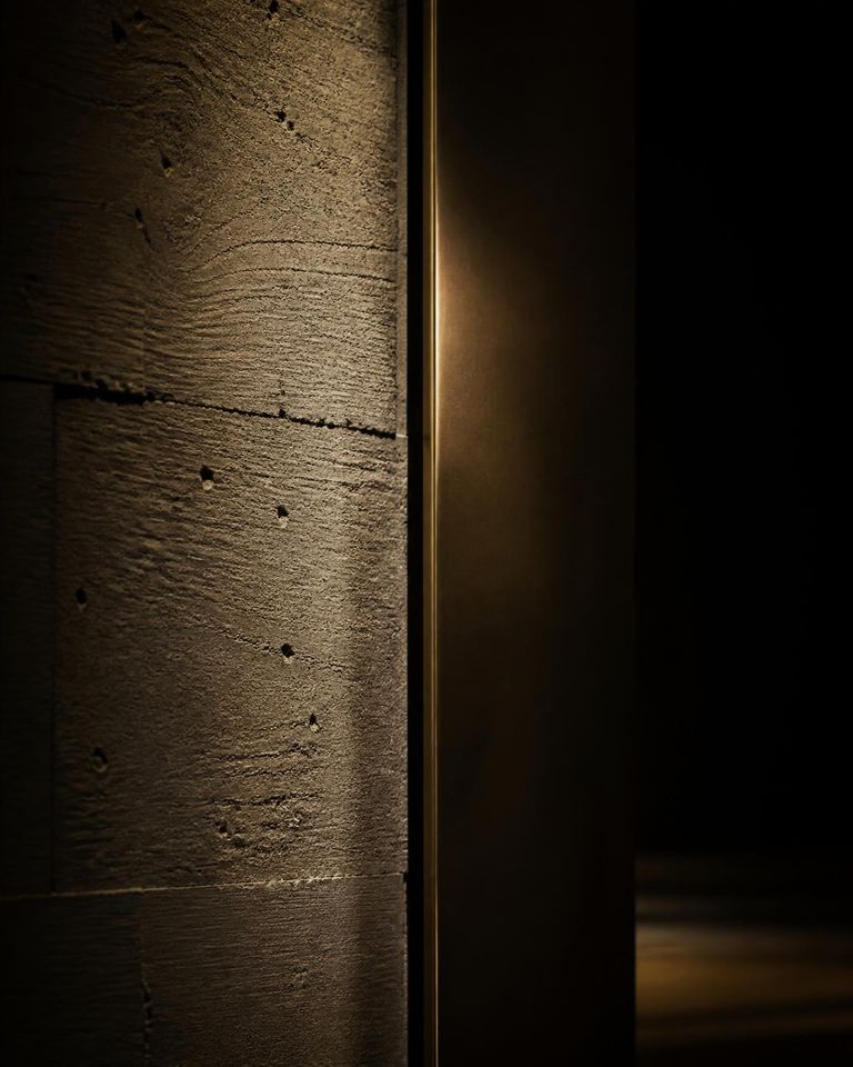 Parede de concreto aparente com um filete de bronze iluminado